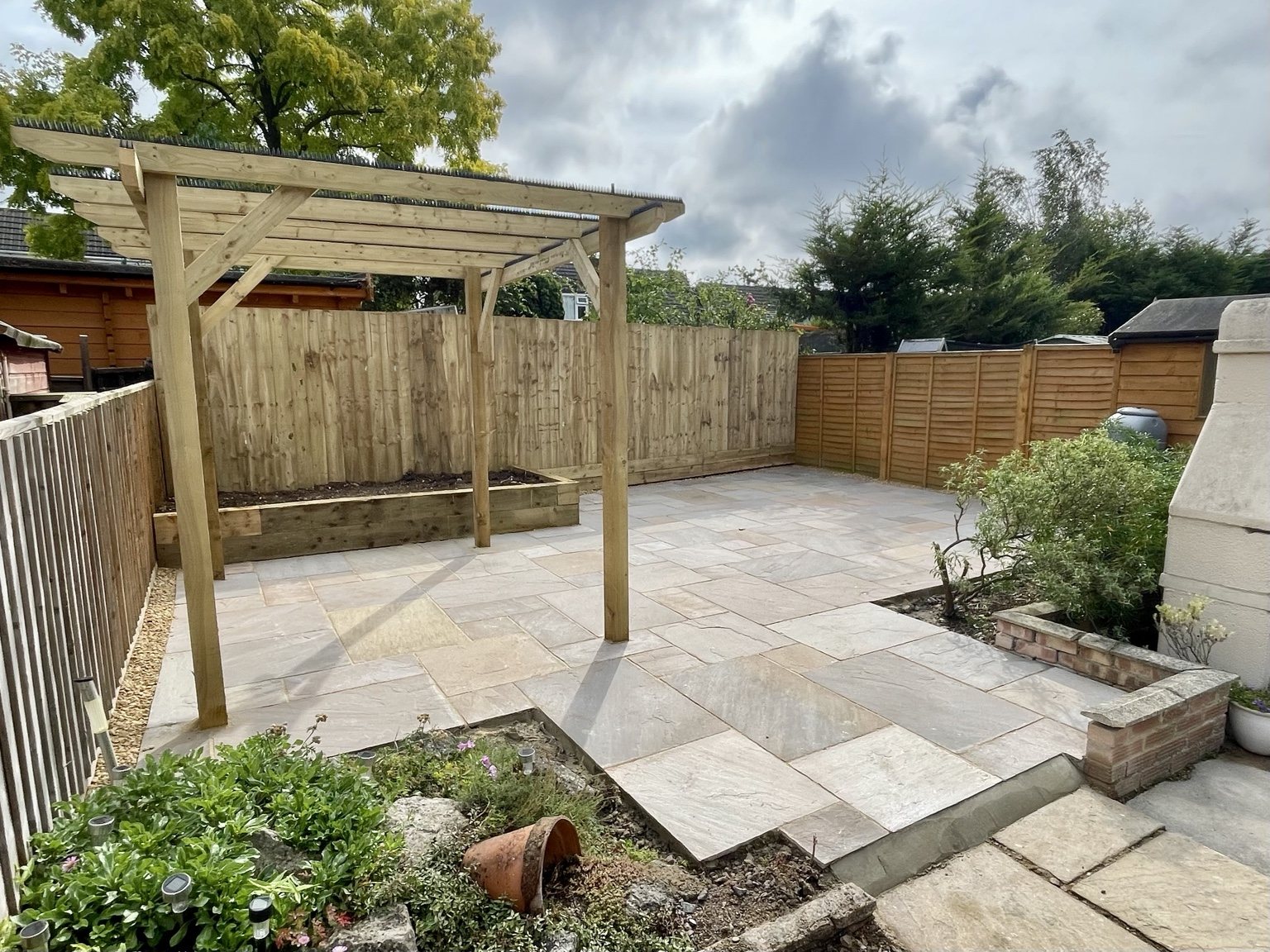 Finished sandstone patio with pergola and raised bed by Stonecrest Paving and Landscaping in Gloucestershire